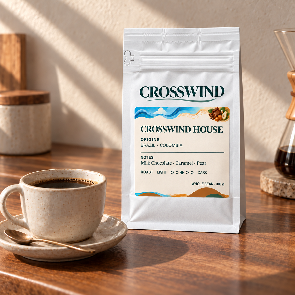 A sealed white Crosswind House coffee bag beside a ceramic cup on a sunlit counter