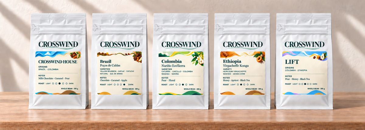 Illustrative lineup of five sealed 300 g Crosswind coffee bags with colourful illustrated labels on an oak counter